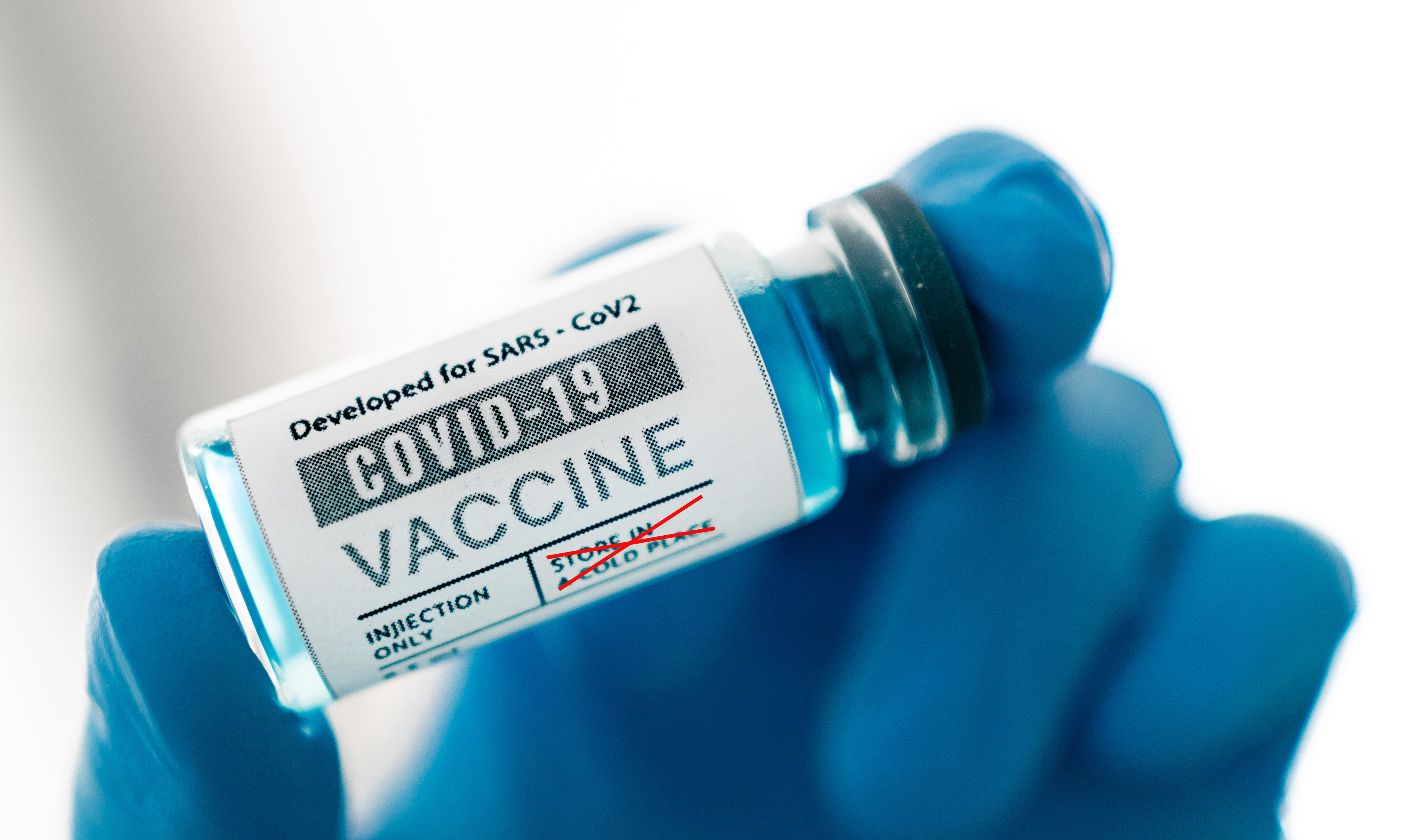 Vial rotulado como vacuna contra la COVID-19 sostenido con guantes azules